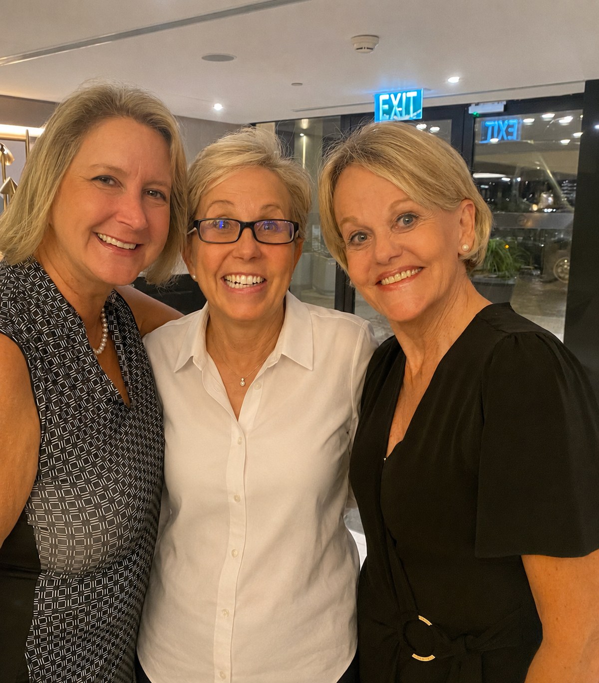 Tanya, Micki, and Cheryl Lynne, close together and laughing in the hotel lobby.